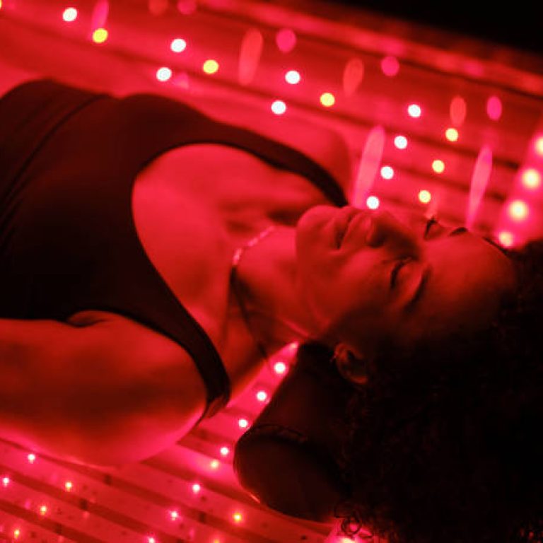 A multiracial woman on an LED light bed, receiving red light therapy.